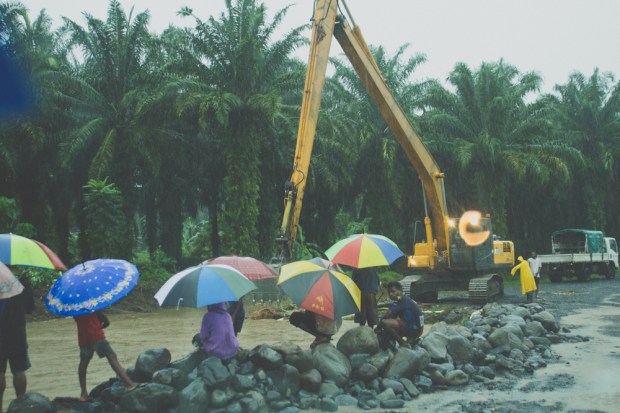People watch as the excavator clears the debris from building up and blocking the flow of water under the bridge 